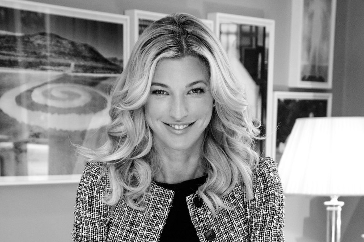 Nicole Junkerman smiling in a tweed jacket, a black and white editorial portrait in a bright room