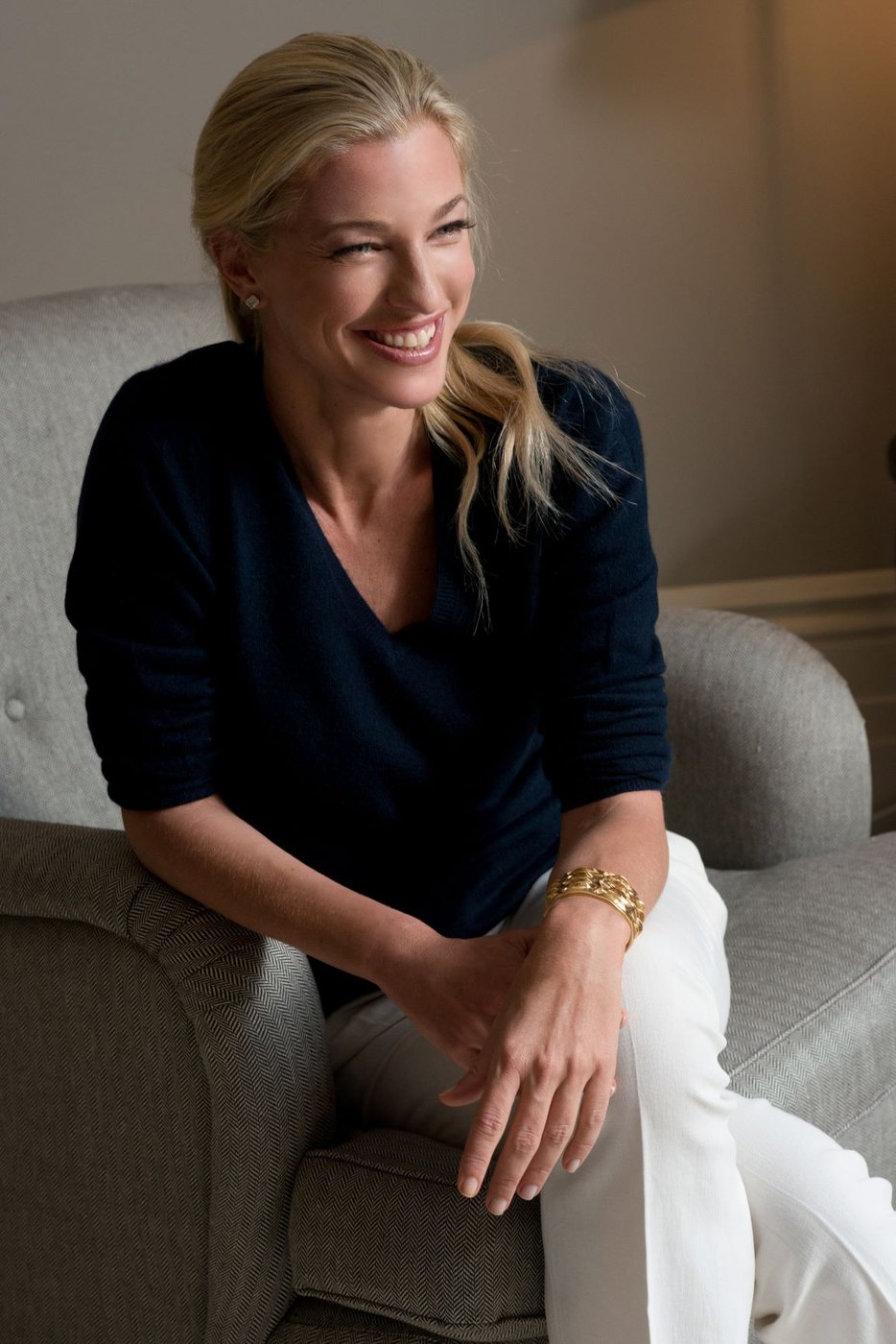 Nicole Junkerman seated on a sofa in a relaxed navy top, smiling during a quiet moment